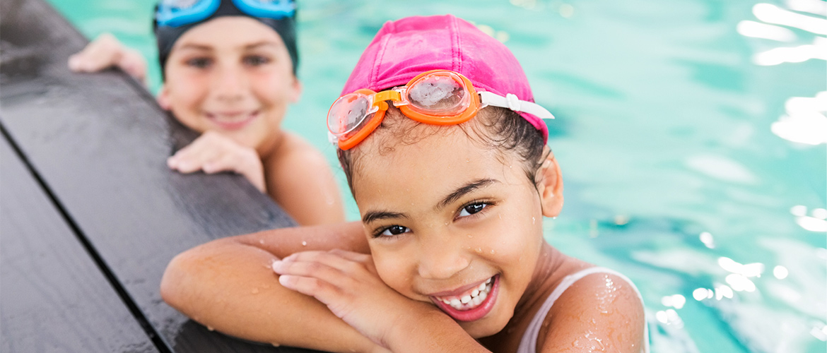 Children smile as they hang on the side of a pool